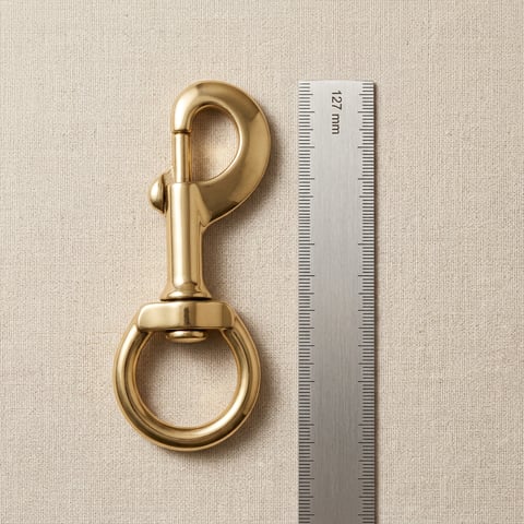 Polished brass round-ring swivel snap hook on linen with measuring scale