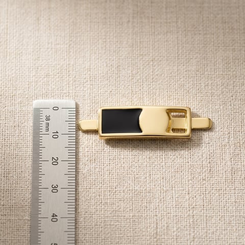 Polished gold bar ornament with black inlay on linen with measuring scale